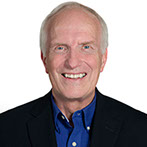 A headshot photo of Dave Jewitt wearing a dark sportsjacket and a dark blue button up shirt.