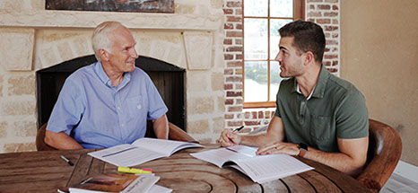 Dave Jewitt, sits at a wooden table next to a fireplace, and discusses Your One Degree with a partipant.