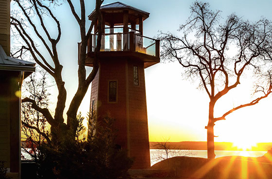 A lookout tower shaped like a lighthouse, shines in the sunset sitting on a property above Grand Lake.